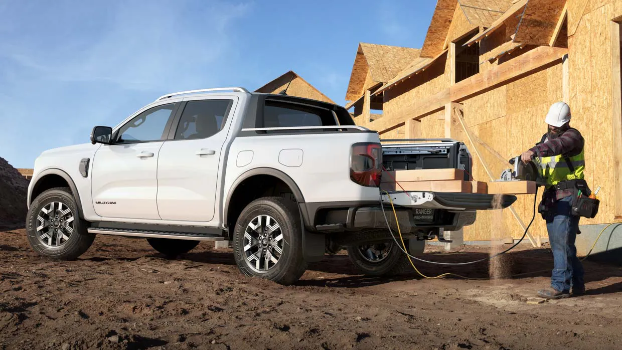 A Ford Ranger Wildtrak plug-in hybrid ute providing AC power for tools on an urban worksite with a tradesman in frame