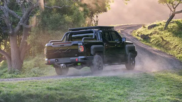 2025 Kia Tasman rear angle driving dirt shot